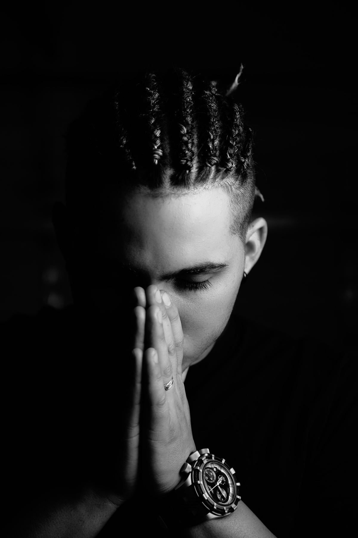 A young man in black and white, head bowed, hands joined.